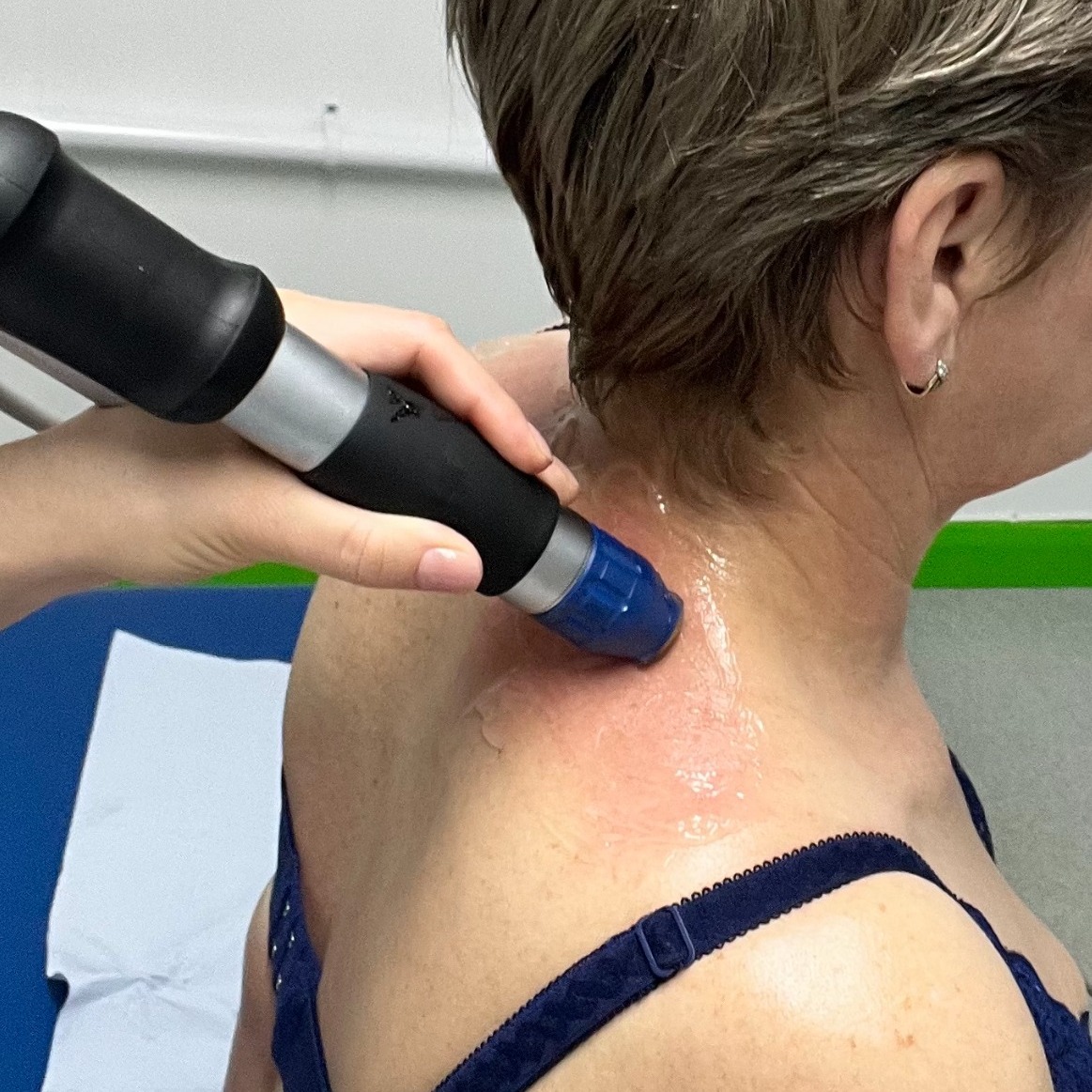 Physiotherapist doing shockwave therapy on the shoulder of a woman.