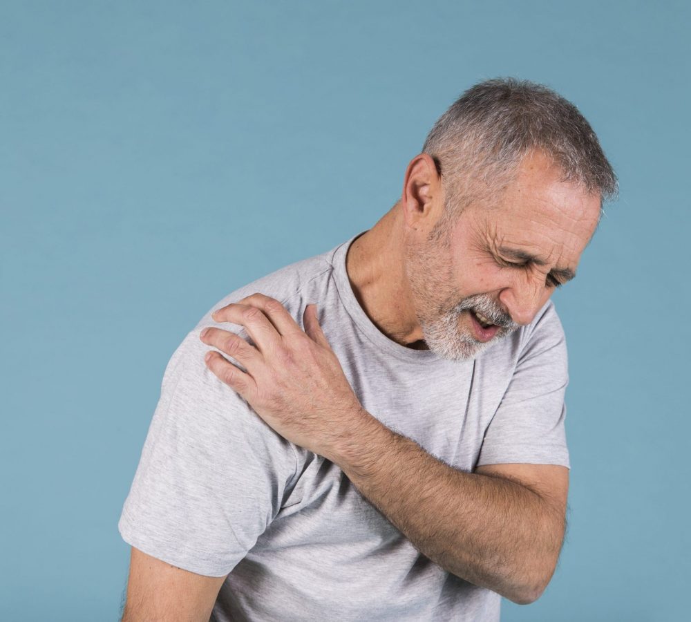 stressed-senior-man-with-shoulder-pain-blue-backdrop